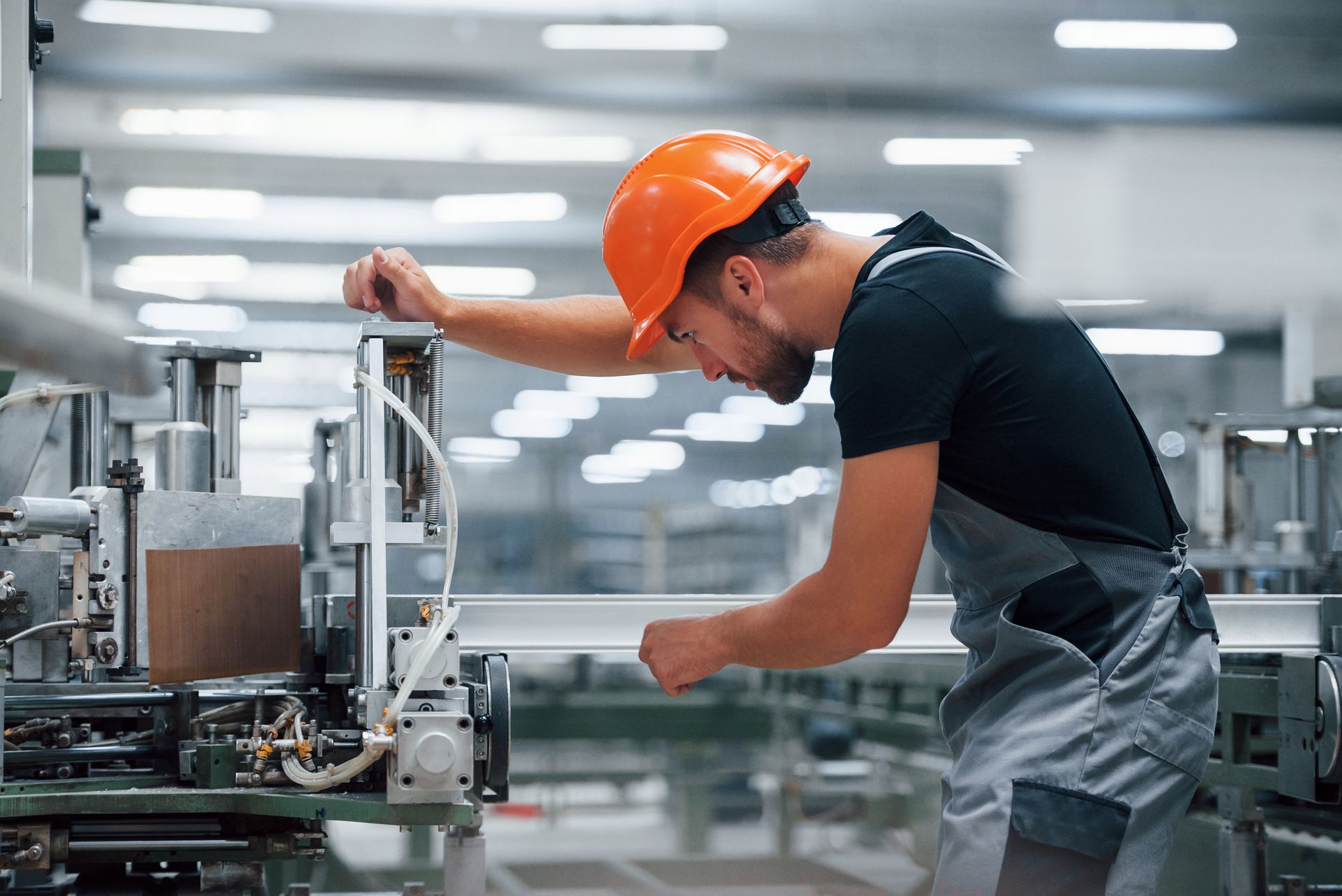 Un technicien au casque orange travaille sur une machine dans un hall de production pour optimiser les processus avec un logiciel ERP.